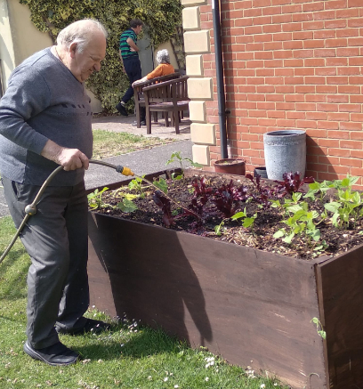 Resident watering plants in a raised planter at Immacolata House Care Home in Somerset
